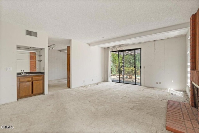 unfurnished living room featuring light carpet, sink, and a textured ceiling