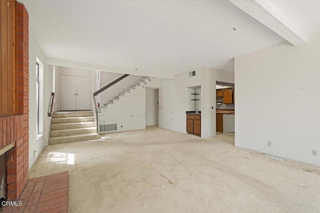 unfurnished living room with light carpet, beam ceiling, a fireplace, and a textured ceiling