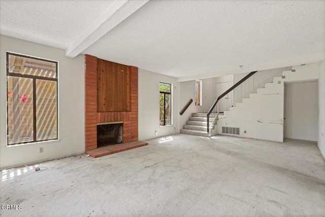 unfurnished living room featuring a textured ceiling, a fireplace, carpet flooring, and beam ceiling