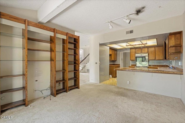 kitchen featuring light carpet, beam ceiling, kitchen peninsula, and a textured ceiling