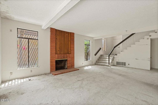 unfurnished living room with carpet floors, a fireplace, beamed ceiling, and a textured ceiling