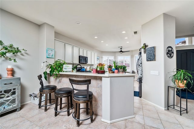 kitchen featuring light tile patterned flooring, a breakfast bar area, range, kitchen peninsula, and white cabinets