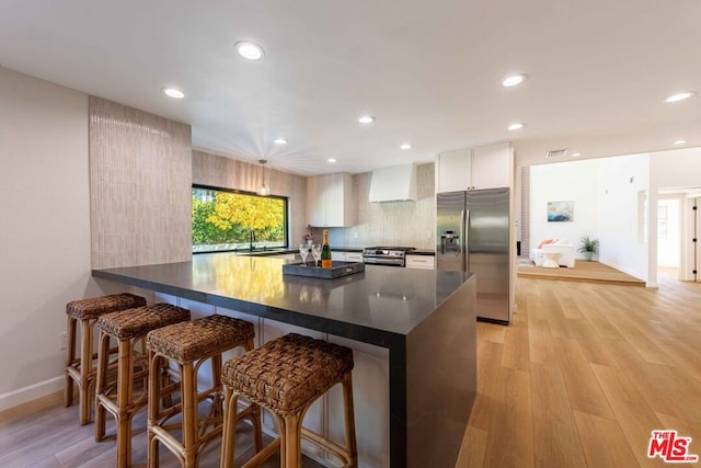 kitchen with white cabinets, stainless steel appliances, premium range hood, a kitchen breakfast bar, and light hardwood / wood-style flooring