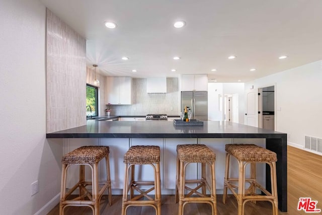 kitchen with appliances with stainless steel finishes, white cabinetry, backsplash, kitchen peninsula, and a breakfast bar area