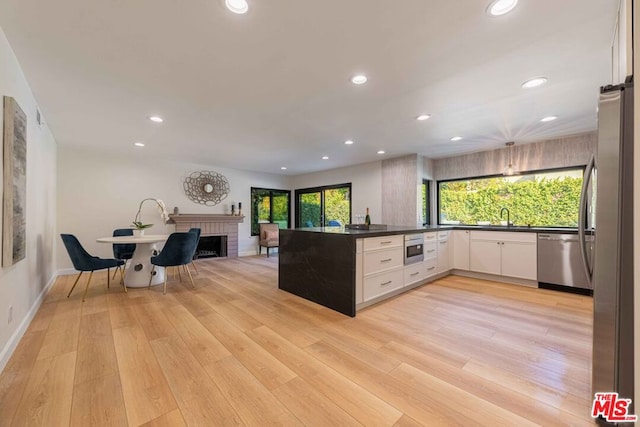 kitchen with white cabinets, stainless steel appliances, kitchen peninsula, light wood-type flooring, and a brick fireplace