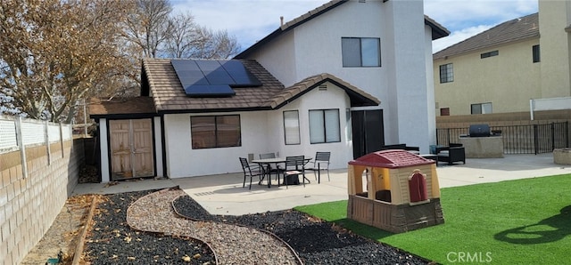 back of house featuring a patio, a fenced backyard, stucco siding, and solar panels
