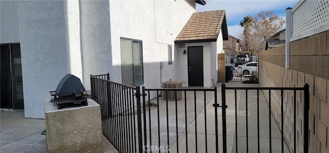 view of exterior entry with a gate, stucco siding, fence, and cooling unit