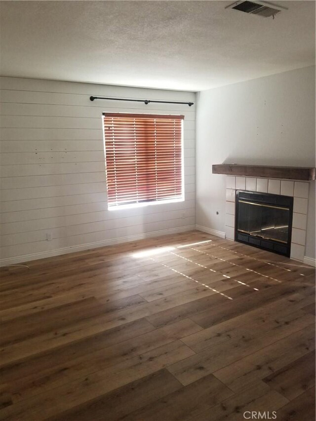 unfurnished living room with a tiled fireplace, baseboards, hardwood / wood-style flooring, and visible vents