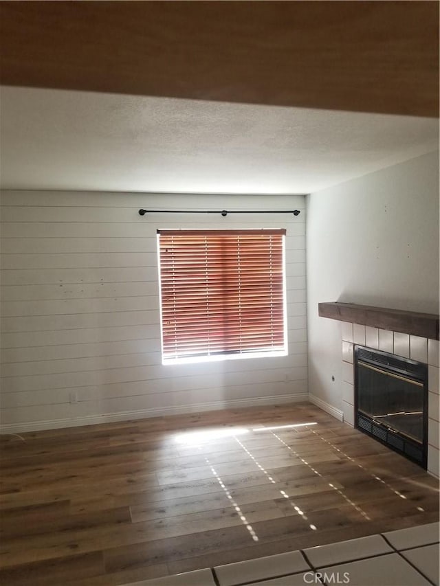 unfurnished living room featuring baseboards, a tiled fireplace, and wood finished floors