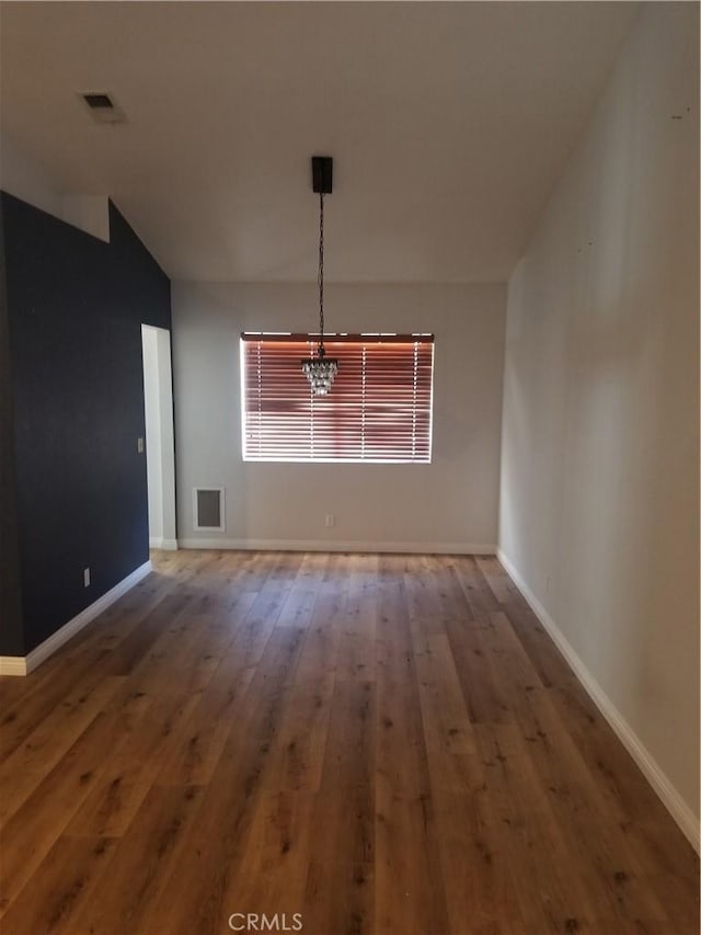 unfurnished dining area with wood-type flooring, baseboards, a notable chandelier, and visible vents