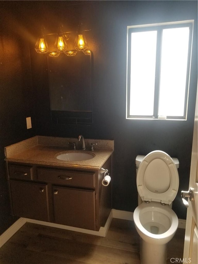 half bath featuring baseboards, plenty of natural light, toilet, and vanity