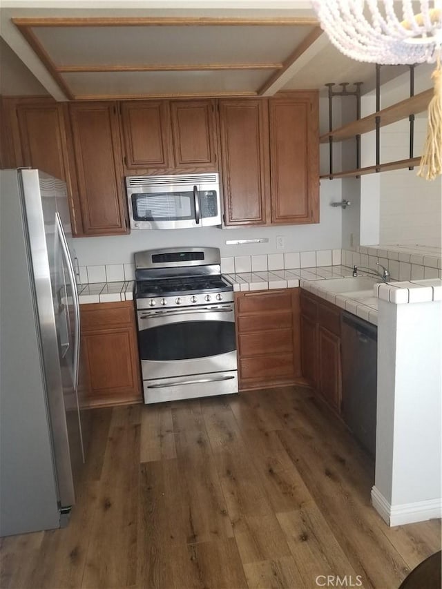 kitchen with brown cabinets, stainless steel appliances, tile countertops, and wood finished floors