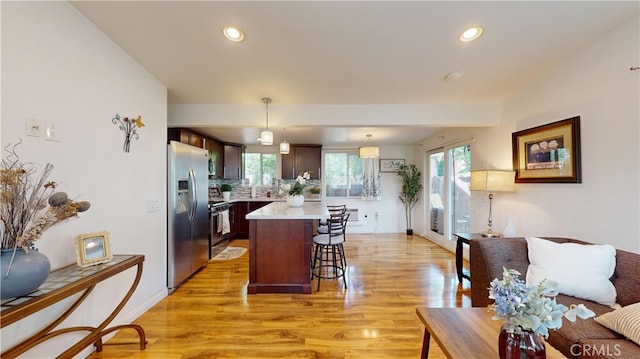 kitchen featuring appliances with stainless steel finishes, a center island, dark brown cabinetry, hanging light fixtures, and light wood-type flooring