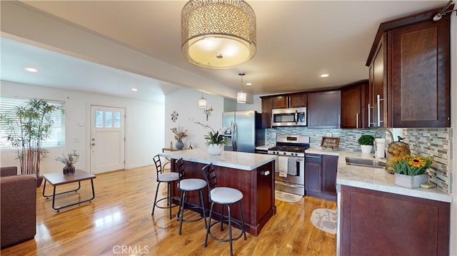 kitchen featuring stainless steel appliances, decorative backsplash, decorative light fixtures, a kitchen island, and sink