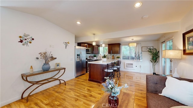 kitchen with appliances with stainless steel finishes, vaulted ceiling, pendant lighting, light hardwood / wood-style flooring, and a center island