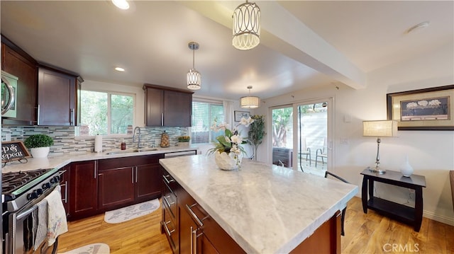 kitchen with appliances with stainless steel finishes, decorative backsplash, hanging light fixtures, a kitchen island, and sink