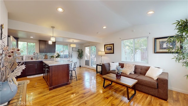 living room featuring lofted ceiling, sink, and light hardwood / wood-style flooring