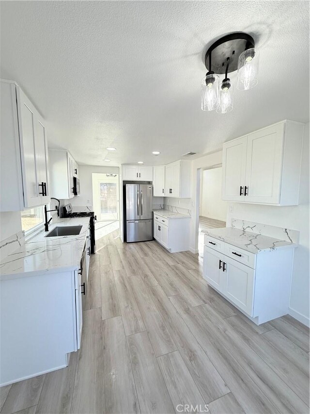 kitchen featuring appliances with stainless steel finishes, light stone counters, white cabinetry, and light hardwood / wood-style floors