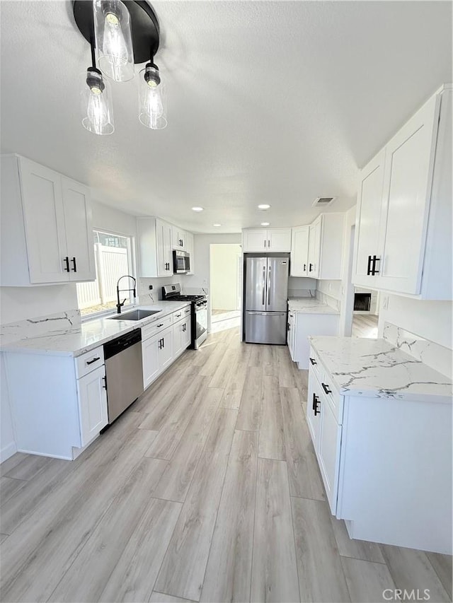 kitchen with white cabinets, stainless steel appliances, sink, light wood-type flooring, and light stone counters