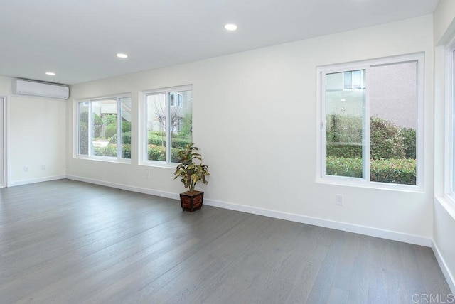 empty room with dark wood finished floors, a wall unit AC, recessed lighting, and baseboards