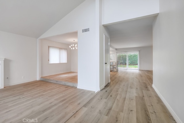 hall featuring high vaulted ceiling, light hardwood / wood-style flooring, and a notable chandelier