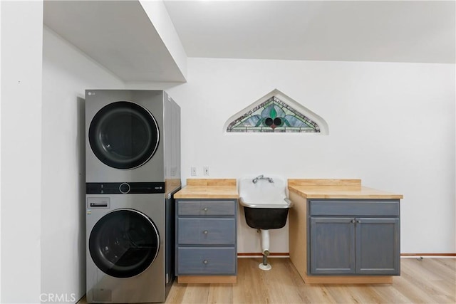 laundry area featuring stacked washing maching and dryer, light hardwood / wood-style flooring, and cabinets