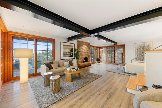 living room featuring light wood-type flooring, a brick fireplace, and beamed ceiling