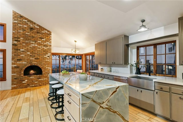 kitchen featuring vaulted ceiling, a brick fireplace, light hardwood / wood-style floors, a kitchen island, and a breakfast bar area