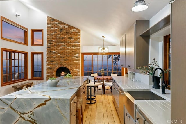 kitchen with light wood-type flooring, a fireplace, vaulted ceiling, a chandelier, and pendant lighting