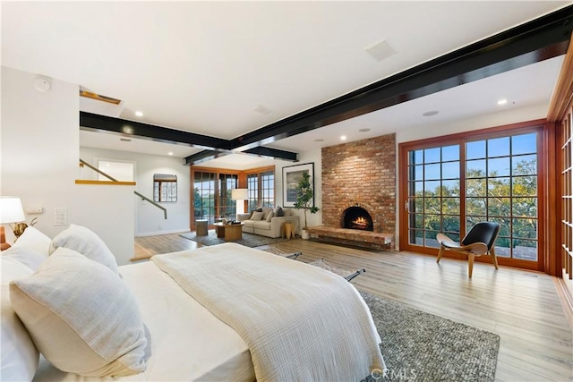 bedroom featuring light hardwood / wood-style floors, beamed ceiling, and a fireplace