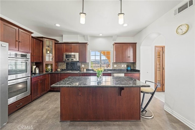 kitchen featuring stainless steel appliances, a center island, decorative light fixtures, dark stone countertops, and sink