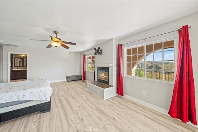 unfurnished bedroom featuring ceiling fan, ensuite bath, multiple windows, and light hardwood / wood-style flooring