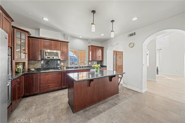 kitchen featuring a center island, decorative light fixtures, stainless steel appliances, dark stone counters, and sink