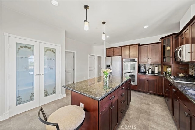 kitchen with hanging light fixtures, appliances with stainless steel finishes, dark stone counters, and a kitchen island