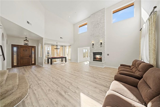 living room featuring a high ceiling, pool table, a stone fireplace, light hardwood / wood-style floors, and a notable chandelier