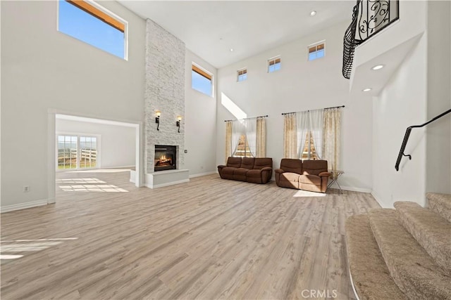 unfurnished living room featuring a fireplace, a towering ceiling, and light hardwood / wood-style floors