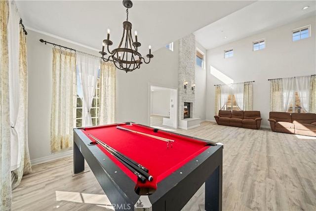 game room with a high ceiling, pool table, an inviting chandelier, a fireplace, and light hardwood / wood-style flooring