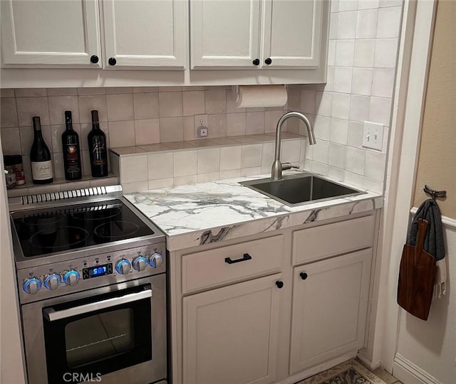 kitchen featuring sink, white cabinetry, backsplash, and high end stove