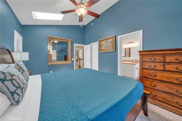 carpeted bedroom featuring ceiling fan, vaulted ceiling with skylight, and connected bathroom