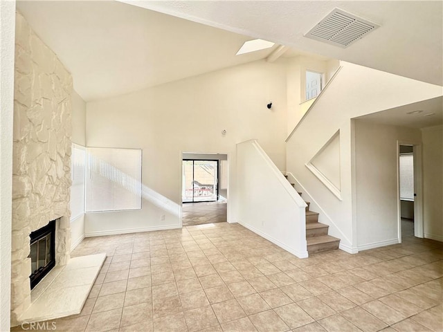 unfurnished living room featuring a skylight, light tile patterned floors, a stone fireplace, high vaulted ceiling, and beamed ceiling