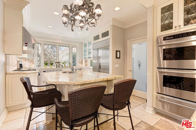 kitchen featuring backsplash, an island with sink, stainless steel appliances, light stone counters, and a chandelier