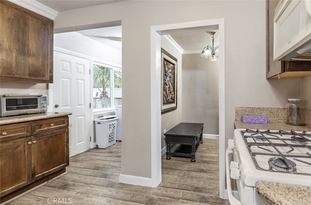 kitchen with a notable chandelier, pendant lighting, white appliances, light wood-type flooring, and ornamental molding