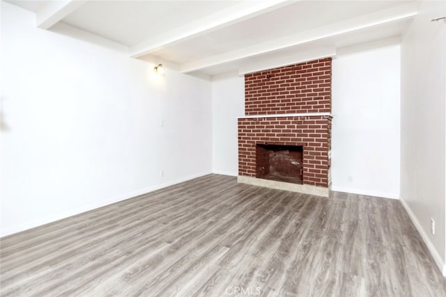 unfurnished living room with a brick fireplace, beamed ceiling, and light hardwood / wood-style floors