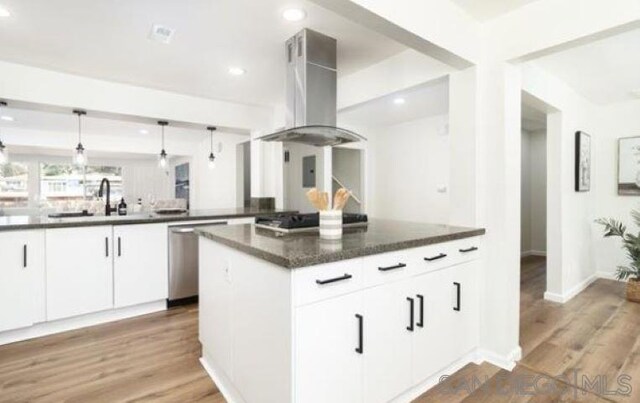 kitchen with pendant lighting, wall chimney range hood, white cabinetry, appliances with stainless steel finishes, and dark stone countertops