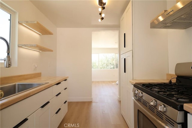 kitchen with range hood, light hardwood / wood-style floors, sink, stainless steel gas range, and white cabinets