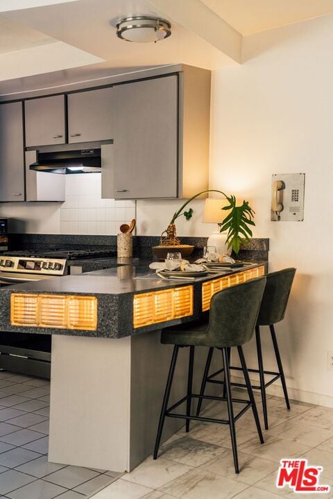 kitchen featuring a kitchen bar, tasteful backsplash, kitchen peninsula, and gray cabinetry