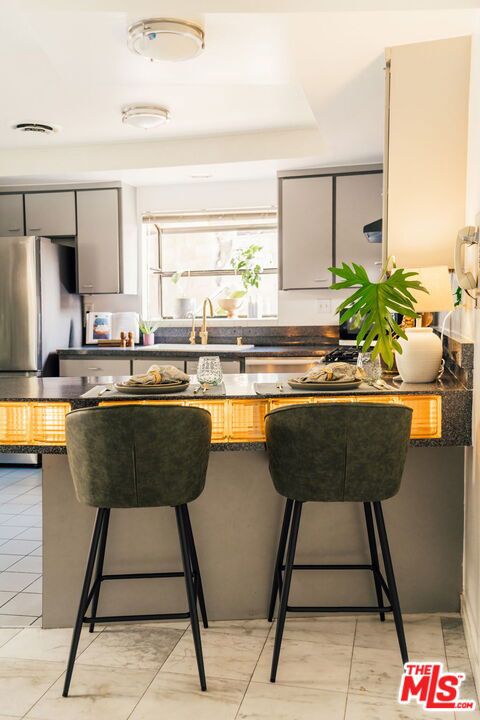 kitchen featuring a breakfast bar area, gray cabinets, stainless steel fridge, and sink