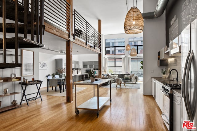 kitchen featuring pendant lighting, a towering ceiling, white cabinetry, stainless steel appliances, and light hardwood / wood-style flooring