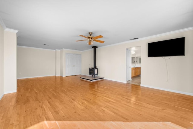 unfurnished living room featuring ornamental molding, a wood stove, ceiling fan, and light hardwood / wood-style floors