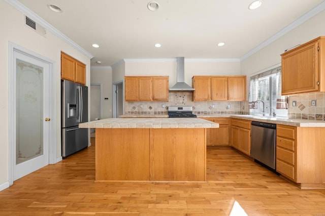 kitchen with wall chimney exhaust hood, tile countertops, a center island, light wood-type flooring, and appliances with stainless steel finishes